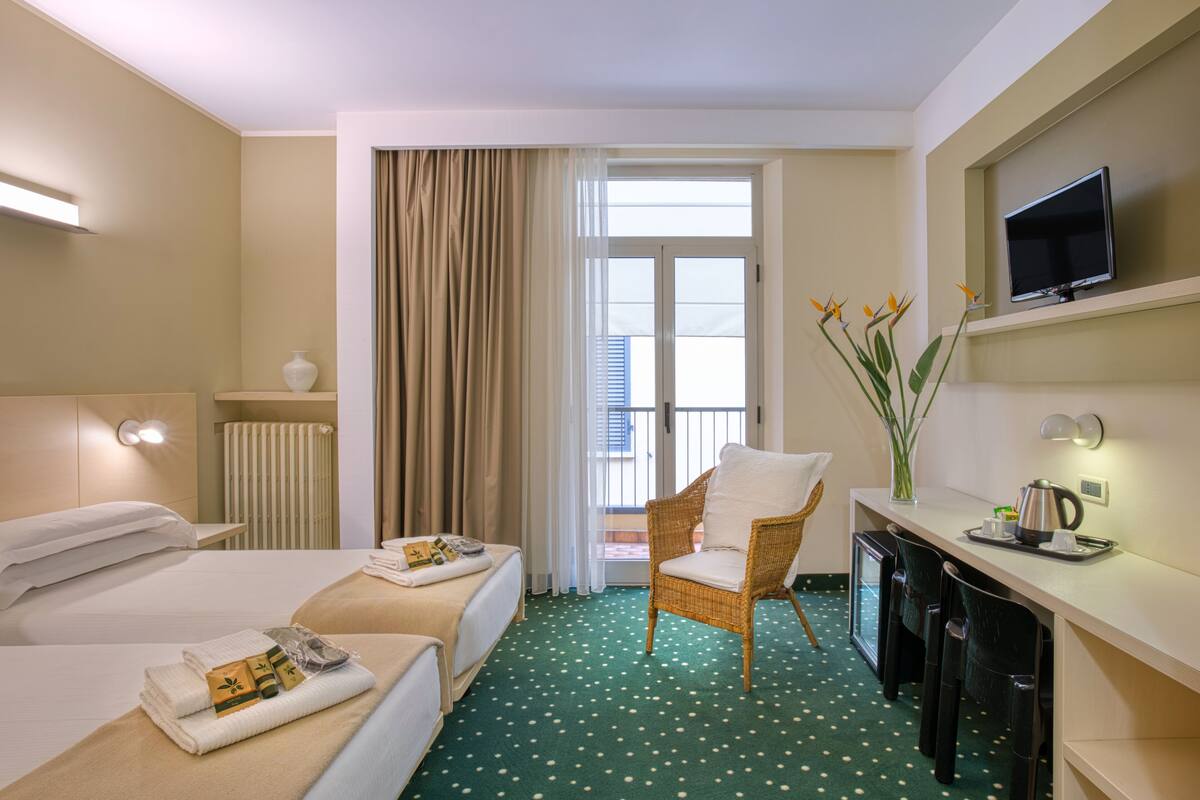 Habitación de hotel con dos camas, un escritorio con televisor, una silla y vistas al exterior.