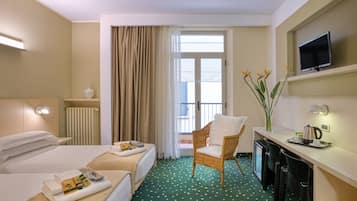 Habitación de hotel con dos camas, un escritorio con televisor, una silla y vistas al exterior.