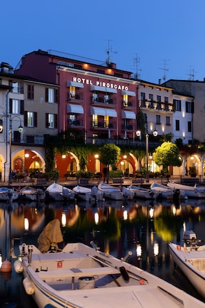 A waterfront hotel with a sign reading "HOTEL PIROSCAPO." Boats are docked in the water in front of the hotel. - Hotel Piroscafo (Desenzano del Garda)
