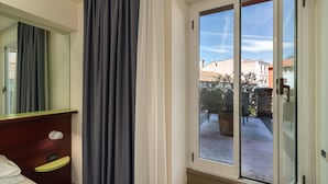 Habitación de hotel con puerta corrediza de vidrio a un patio, una mesita de noche de madera con lámpara y un espejo grande en la pared.