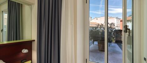 Habitación de hotel con puerta corrediza de vidrio a un patio, una mesita de noche de madera con lámpara y un espejo grande en la pared.