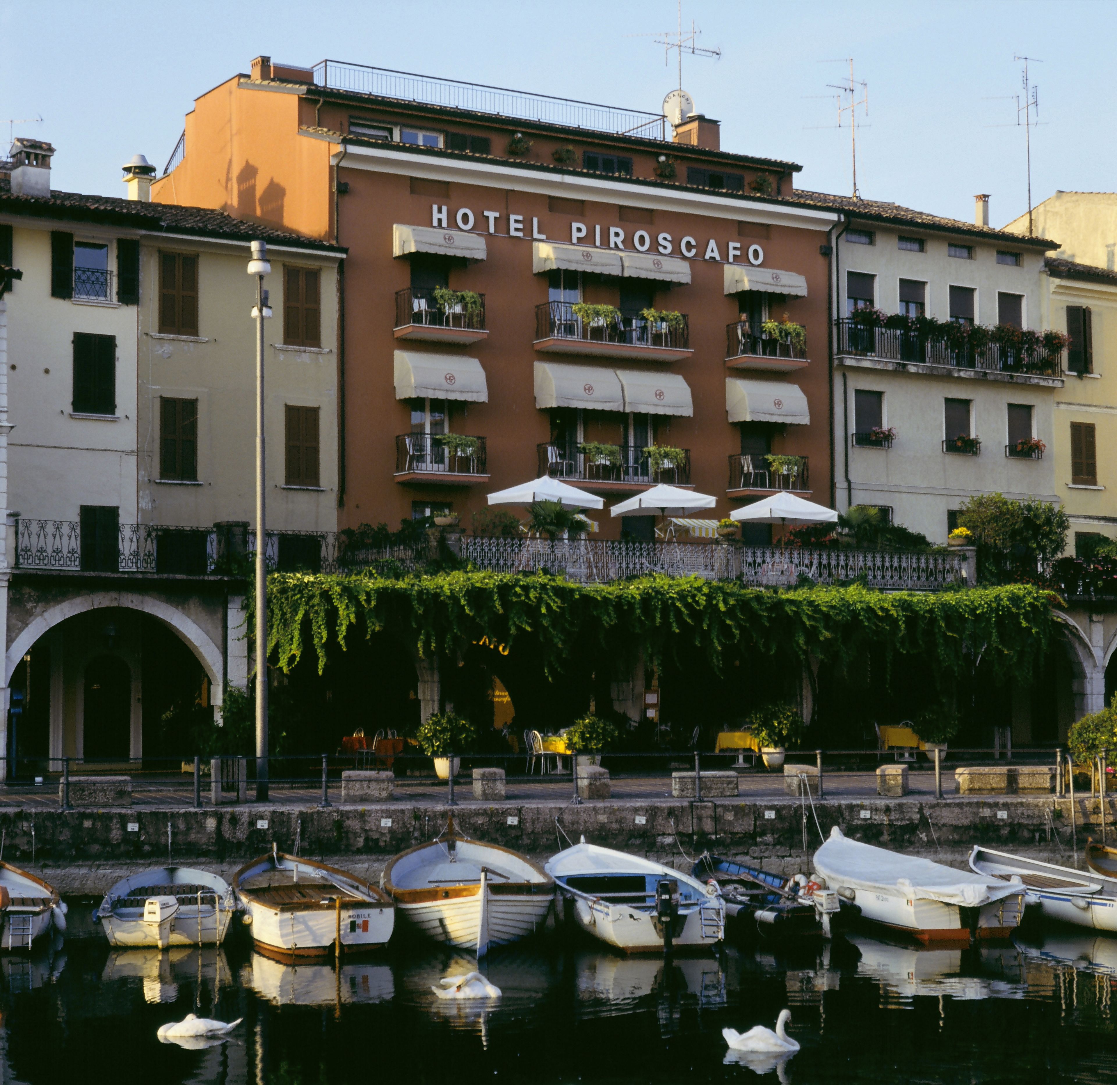 A hotel with a sign reading "HOTEL PIROSCAFO" and a waterfront view with boats docked.