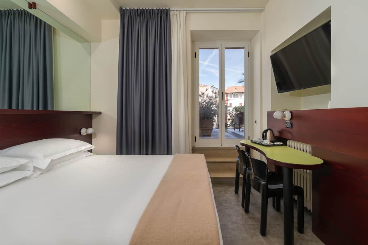 Una habitación de hotel con cama, escritorio con silla, televisión y ventana con cortinas.