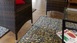 Un salón con muebles de mimbre, una mesa de centro de vidrio y una alfombra estampada.