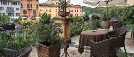 An outdoor patio with wicker furniture, a table with a tablecloth, and potted plants.
