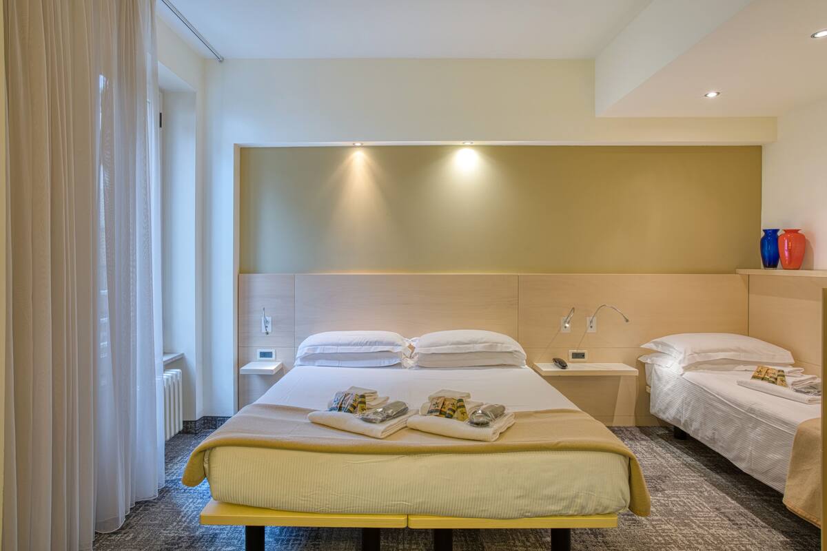 Una habitación de hotel con una cama grande, mesitas de noche y una ventana con cortinas.