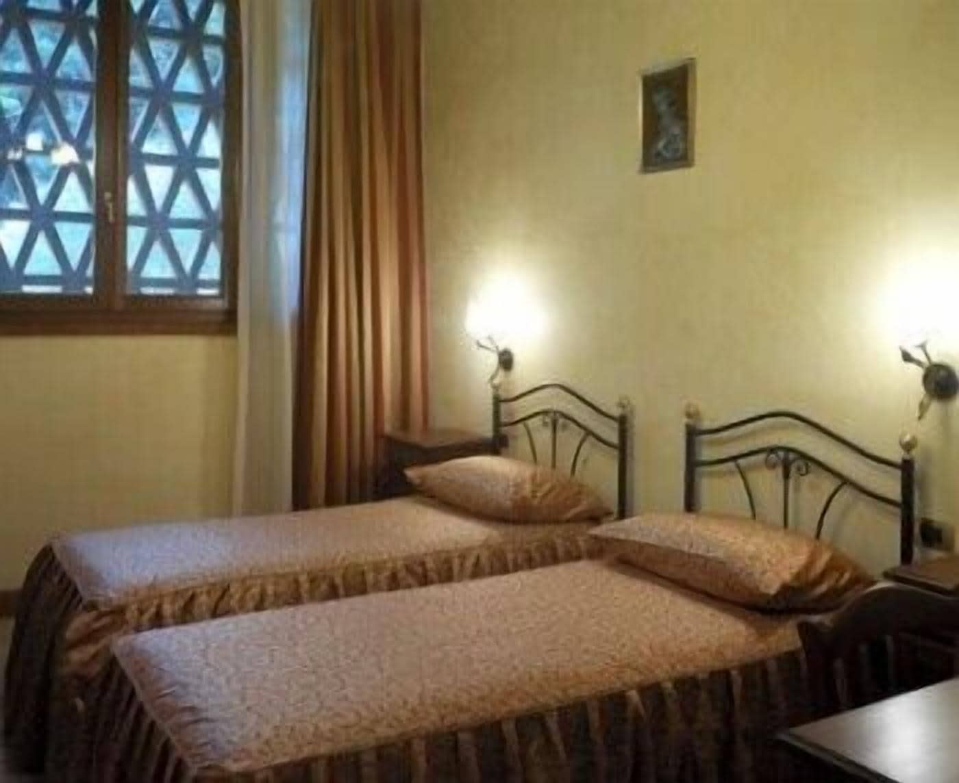 A room with two single beds, a window with a lattice design, and a wall-mounted picture.