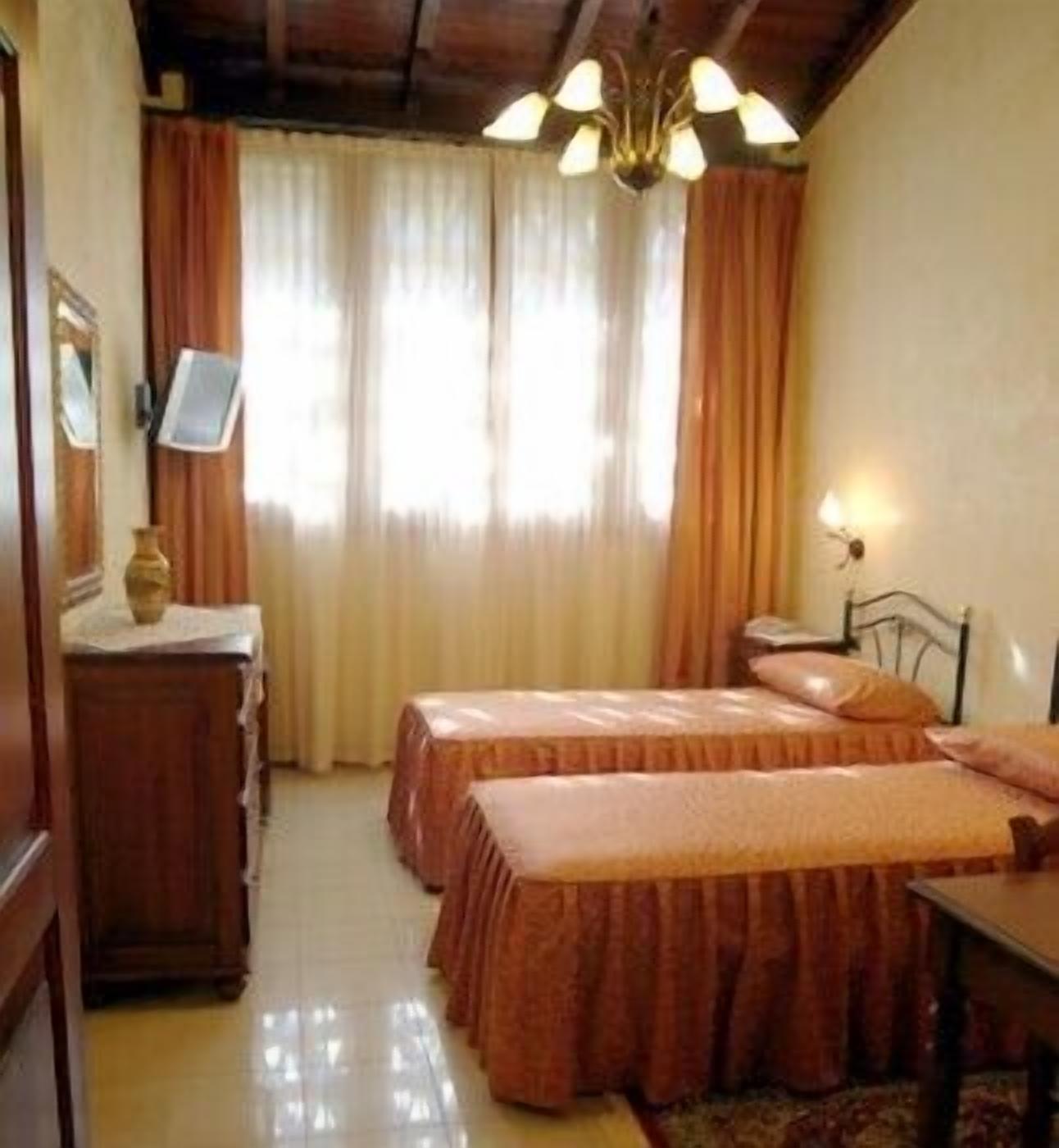 Quarto com duas camas, penteadeira de madeira, espelho e lustre.