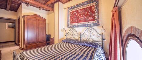 A bedroom with a large bed, wooden wardrobe, and a decorative tapestry on the wall.