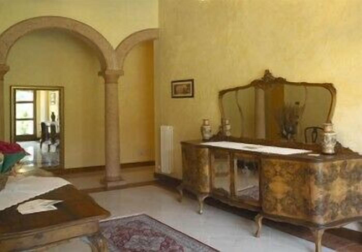 A room with a marble vanity, a mirror, and a wooden chair. There is a doorway leading to another room.