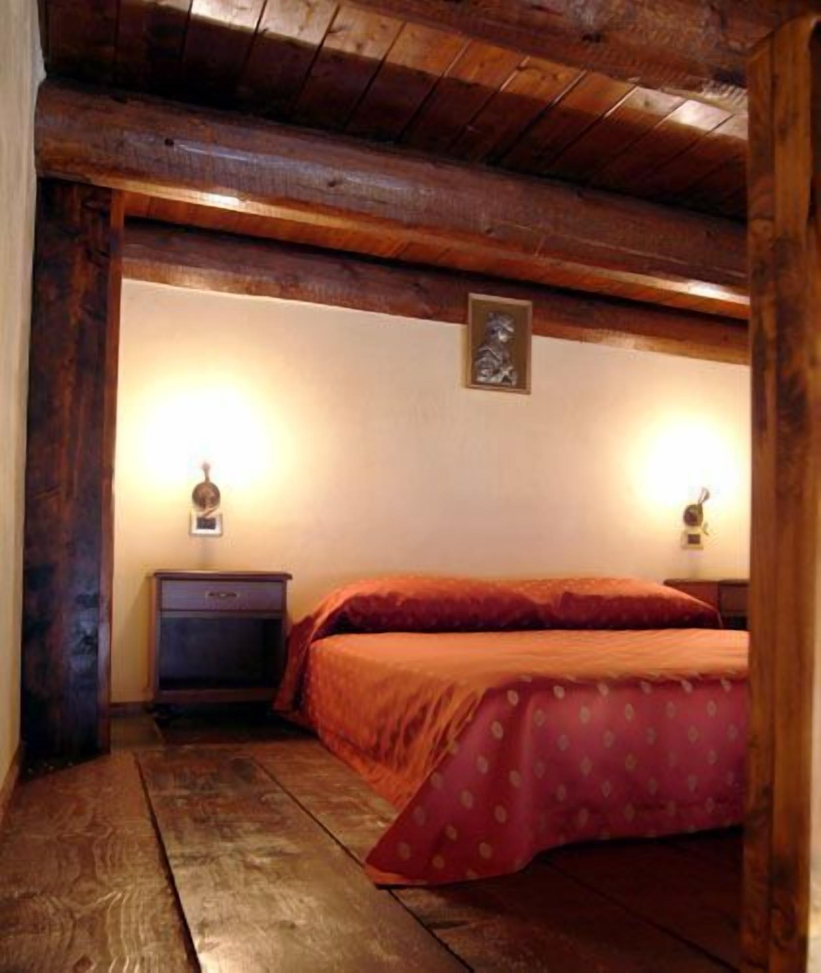 A bedroom with a wooden ceiling, a bed with a red bedspread, two bedside lamps, and a small nightstand.