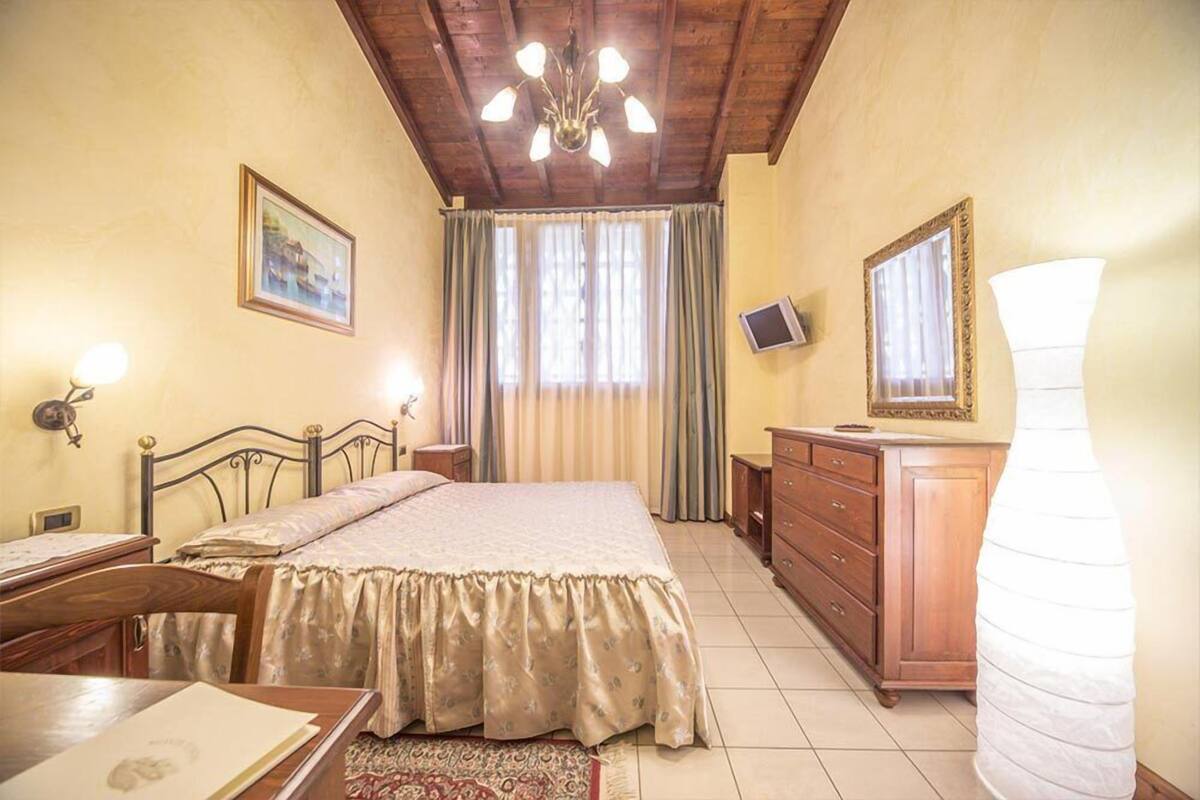 Une chambre à coucher comprenant un lit, une commode en bois, un bureau, une chaise, un miroir, un téléviseur et un lustre.