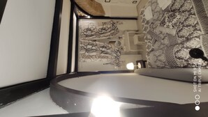 Un baño moderno y compacto, con un tocador curvo, un espejo y baldosas estampadas.
