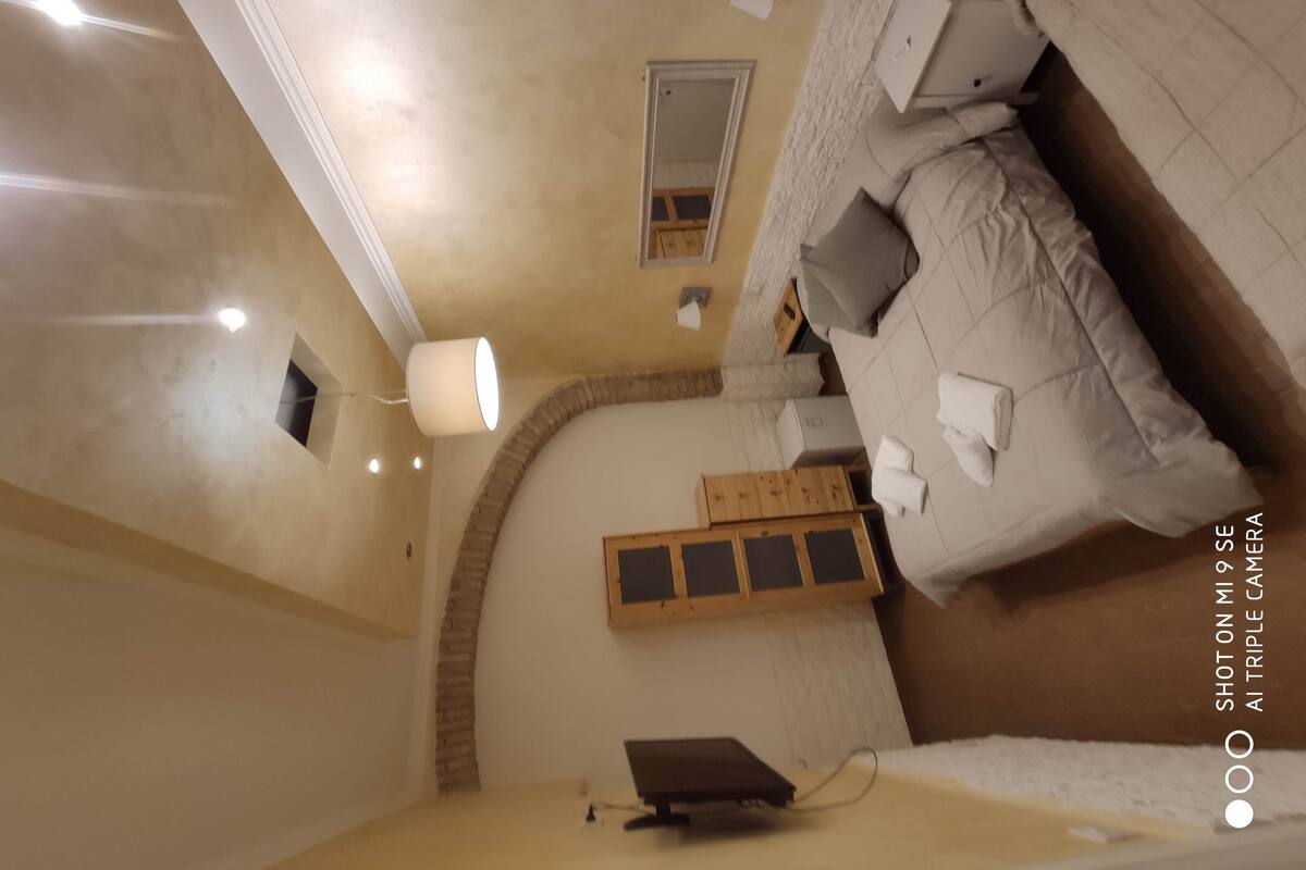 A room with a bed, a small desk, a lamp, and a wall-mounted mirror.