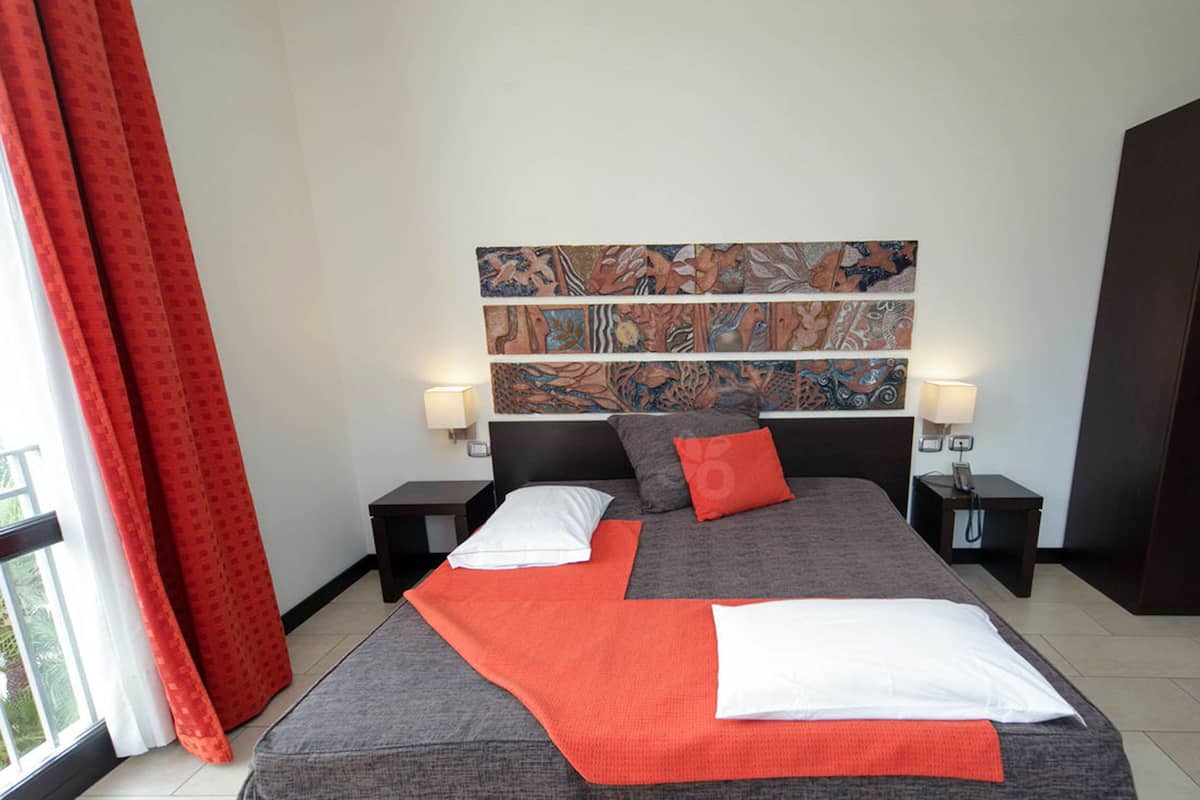 A hotel room with a large bed, two bedside tables, a nightstand, a red curtain, and a wall with colorful artwork.