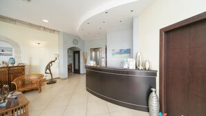 A reception area with a curved reception desk, a wooden bench, and a decorative sculpture. - Al Ritrovo Ristorante & Albergo (San Vito Lo Capo)