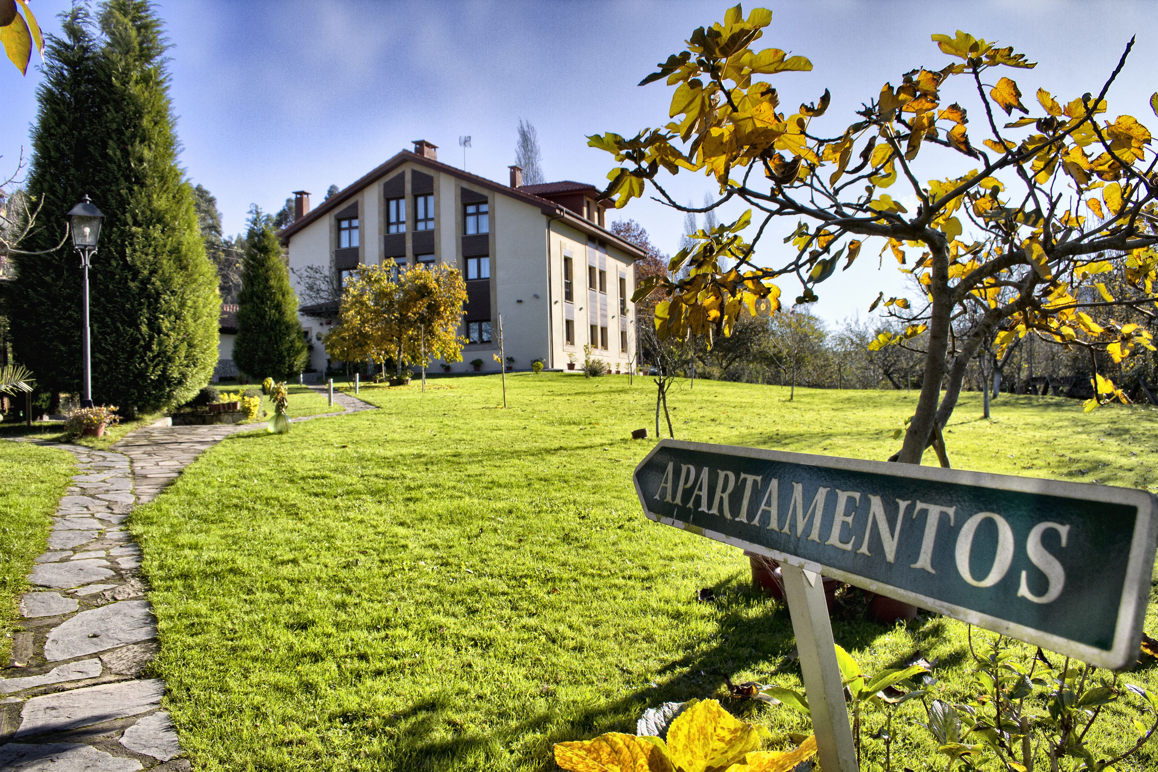 A well-maintained lawn, a stone pathway, and a building with a sign reading "APARTAMENTOS".