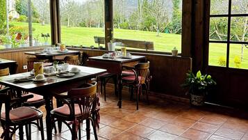 A dining area with wooden tables and chairs, a view of a garden, and a brick wall.