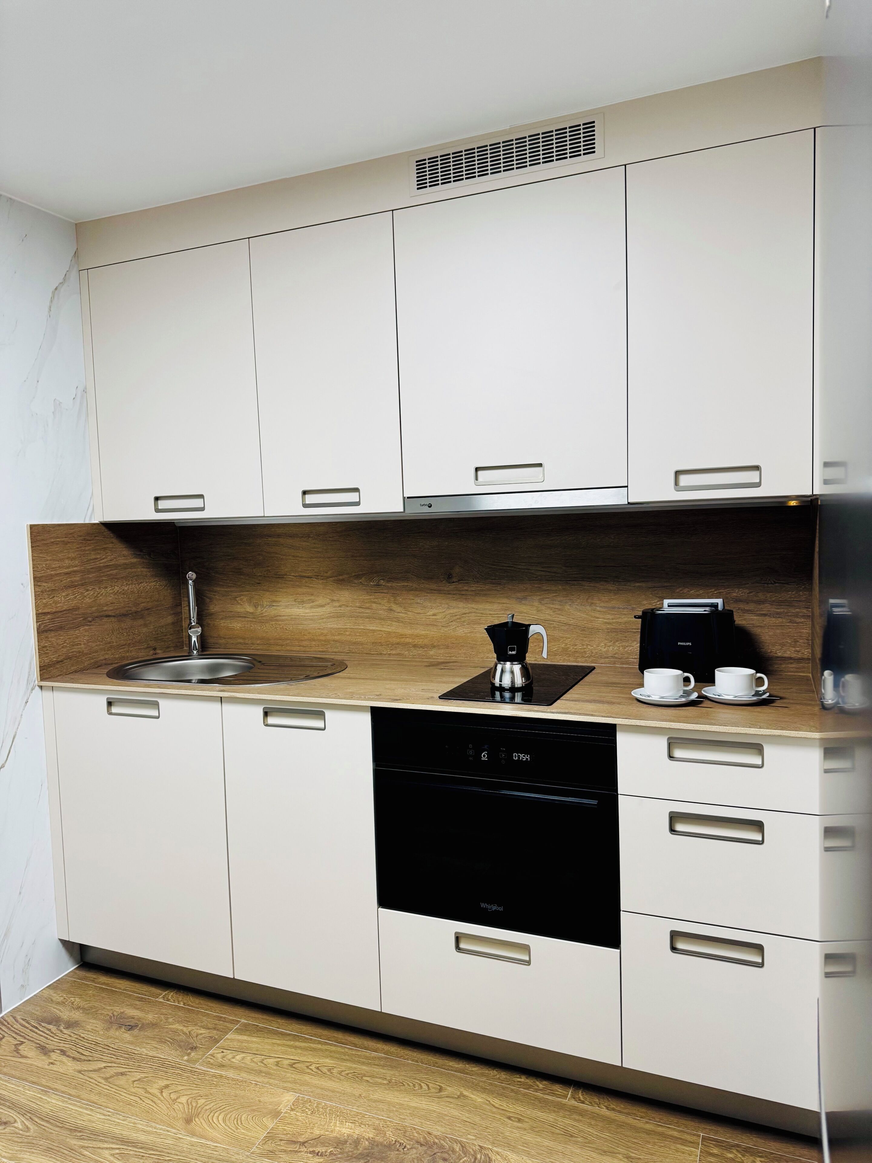 Une cuisine moderne avec des meubles blancs, un plan de travail en bois, un évier, un lave-vaisselle et une machine à café.