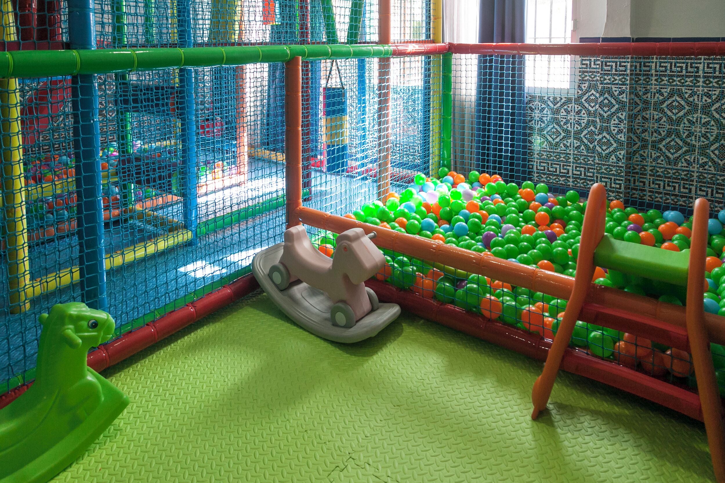 Un espace de jeux pour enfants avec une piscine à balles, un cheval à bascule et une structure d’escalade.