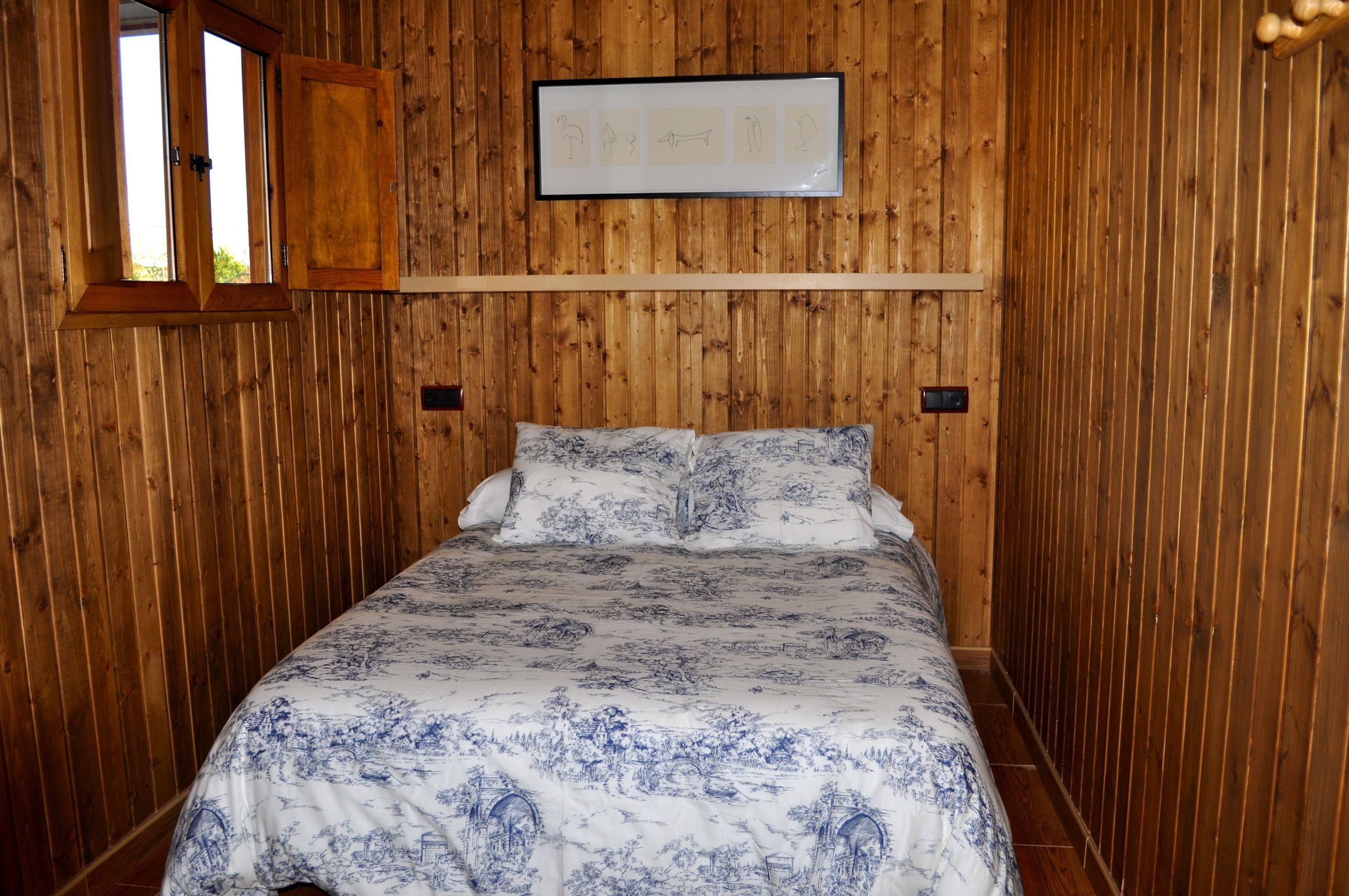 Una habitación con paneles de madera, una cama, un ventanal y un cuadro en la pared.
