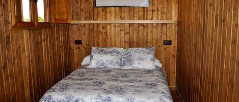 Una habitación con paneles de madera, una cama, un ventanal y un cuadro en la pared.