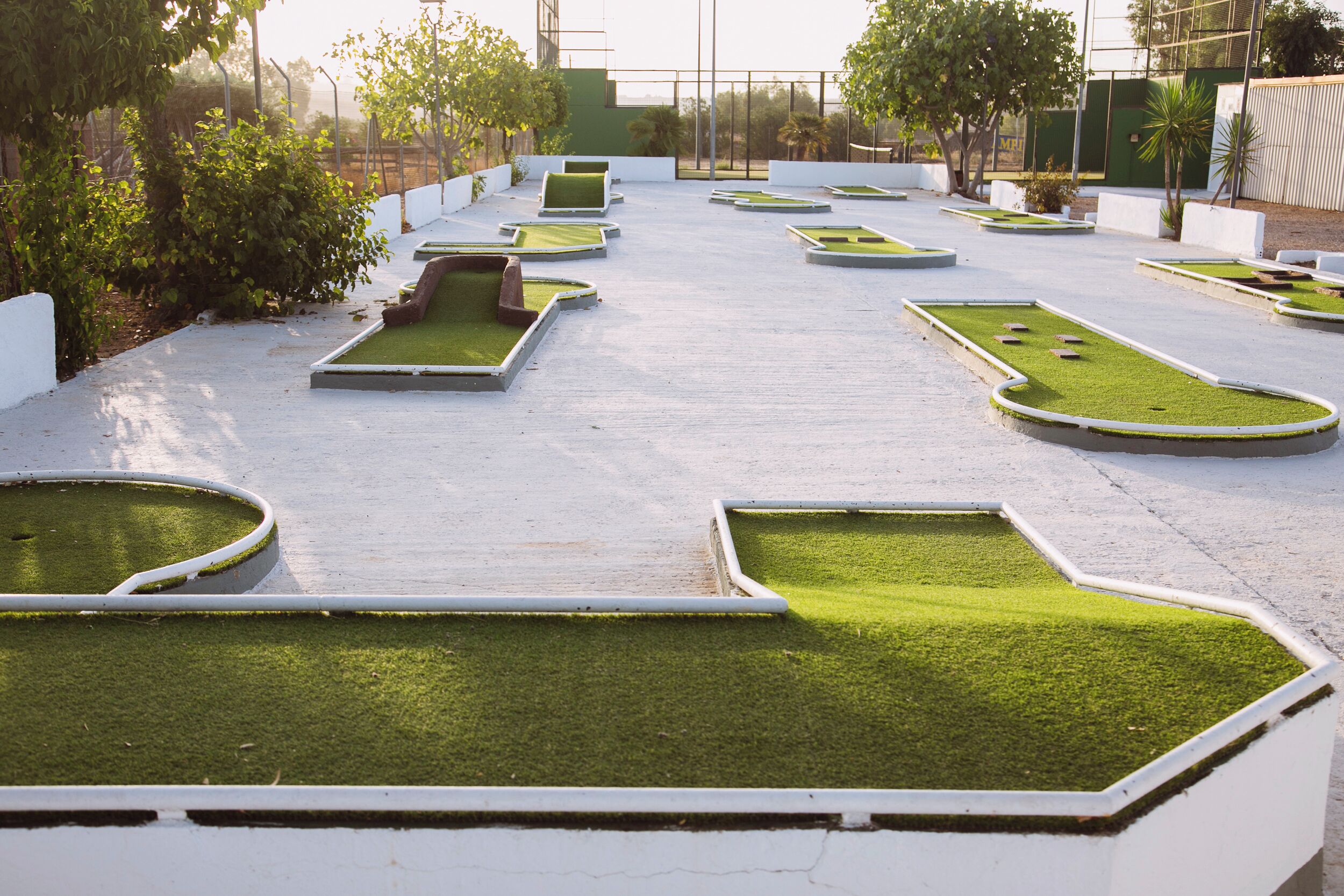 A rooftop garden with multiple rectangular planters containing green grass, surrounded by white walls and a metal fence.