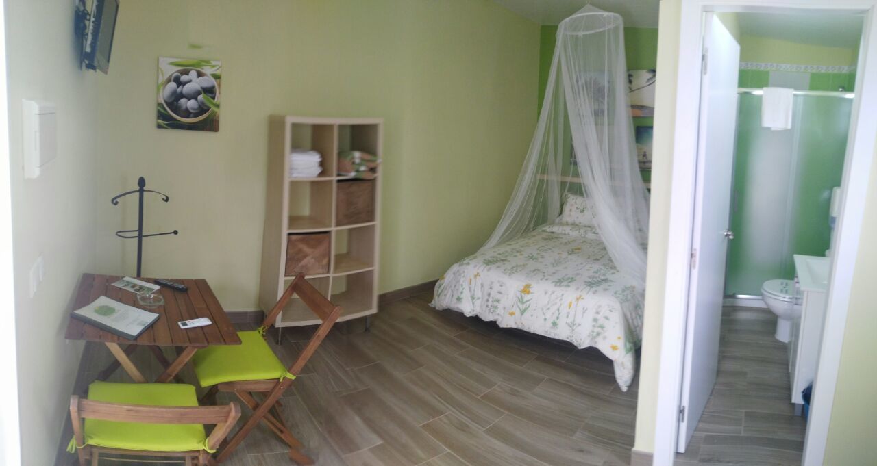 Un dormitorio con cama, escritorio y sillas, armario y baño visible a través de una puerta abierta.