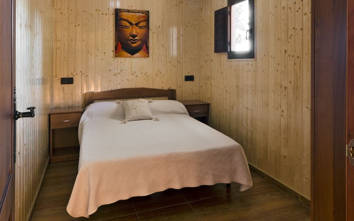 Un dormitorio con pared de madera, una cama con colcha blanca, una mesita de noche y un cuadro colgado en la pared.