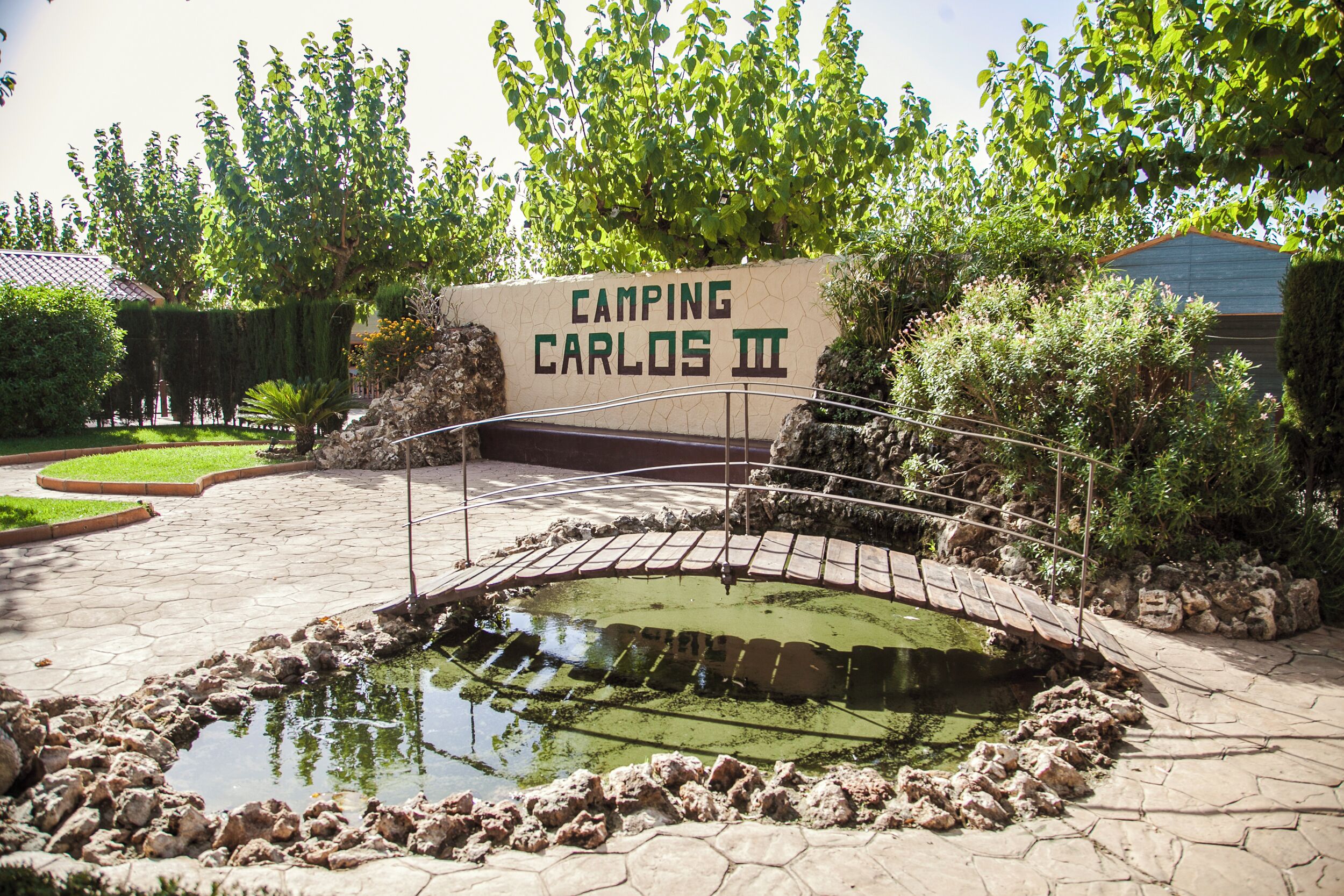 Naamplaatje voor 'Camping Carlos II' met een brug over een vijver.
