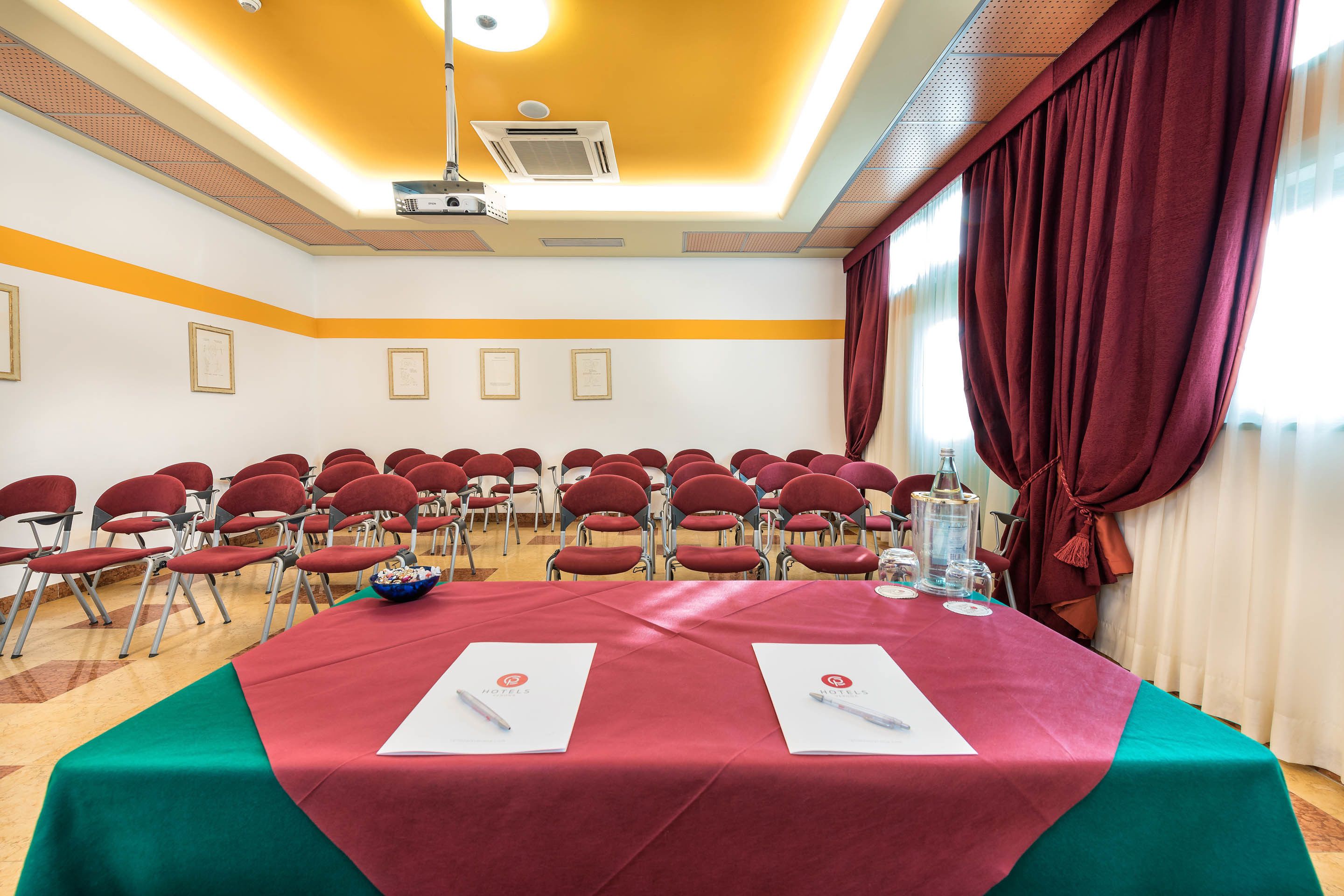 Ein Konferenzraum mit rotem Tisch, Stühlen und einem Projektor.