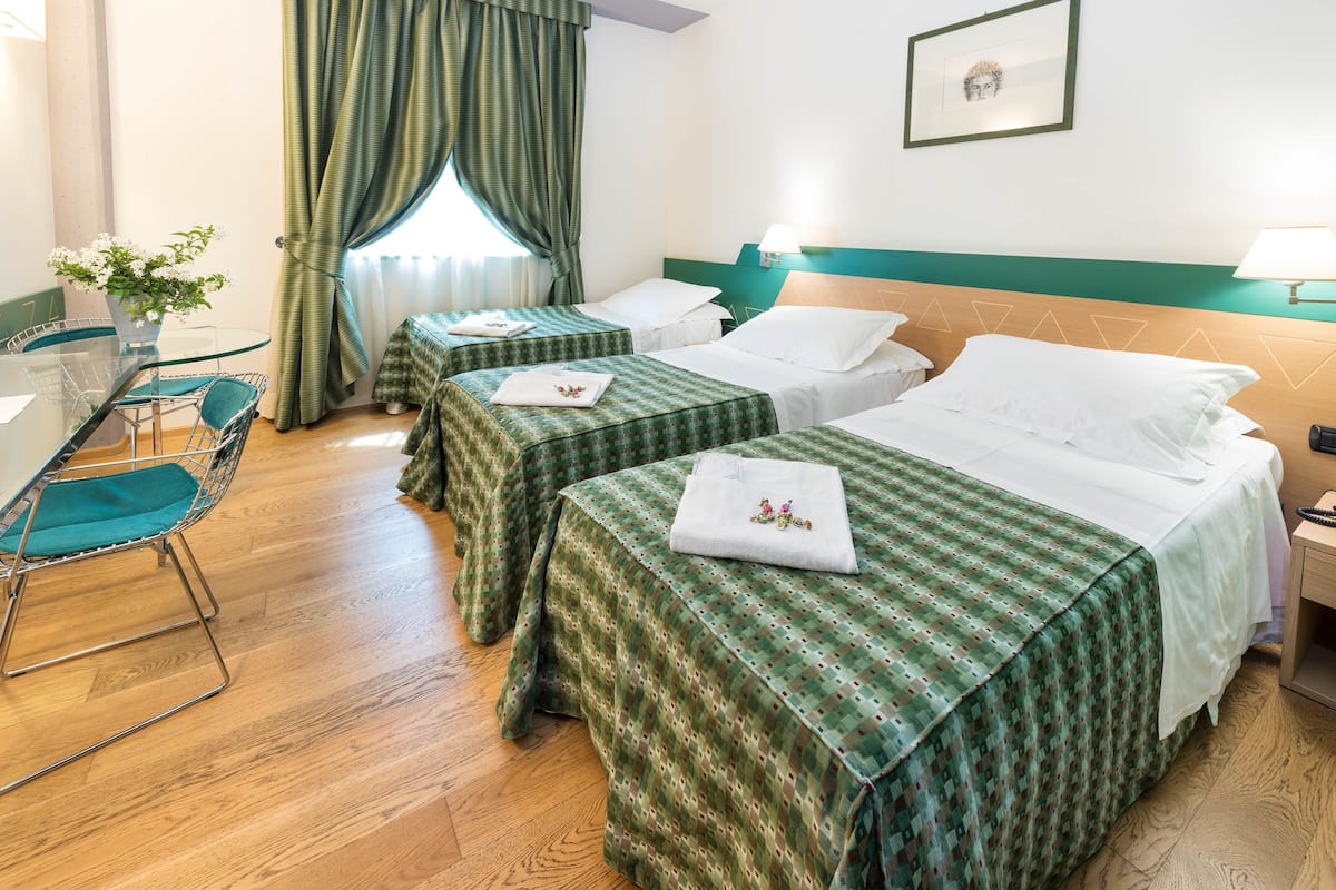 Habitación de hotel con dos camas individuales, una mesita con una silla y una ventana con cortinas.