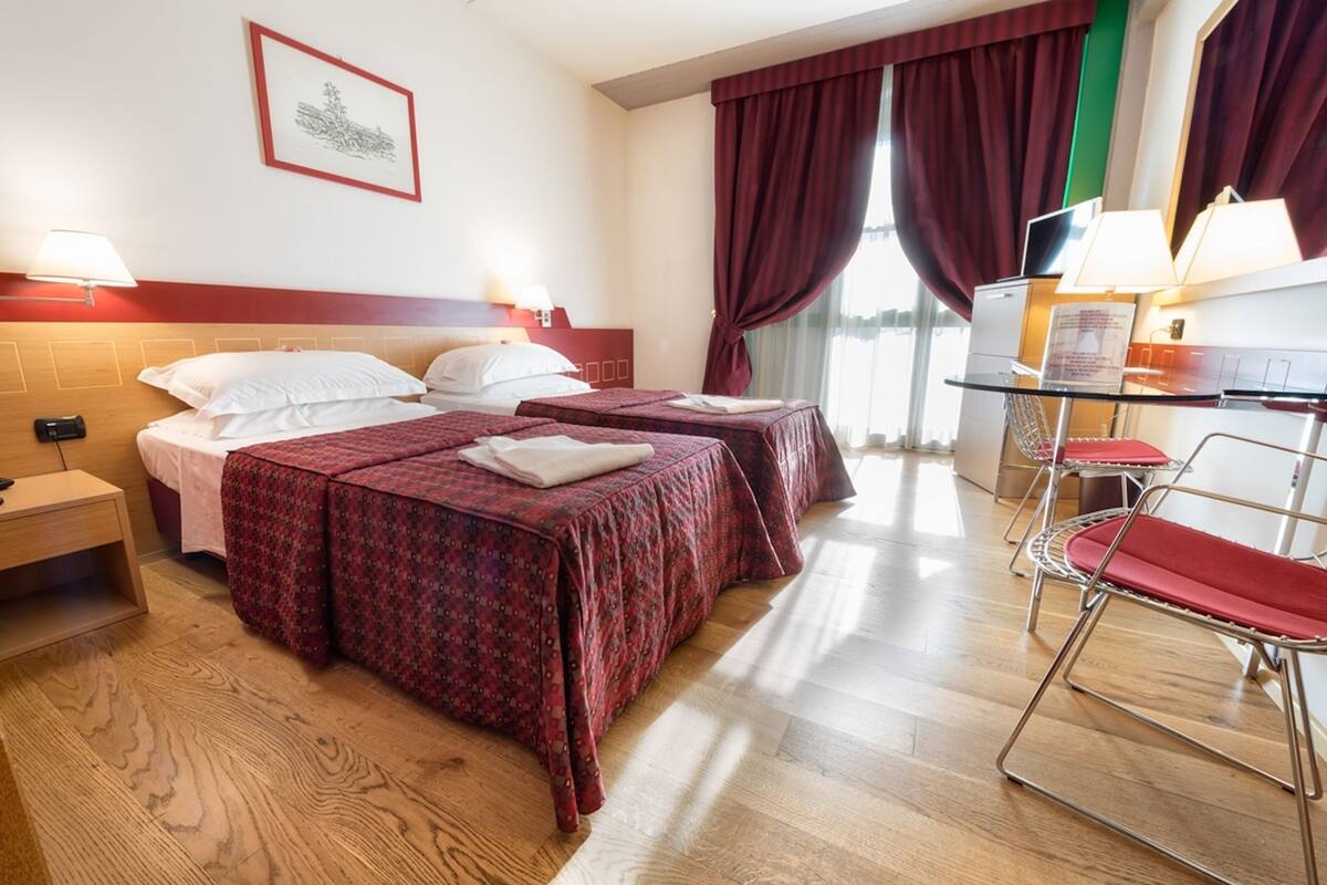 Habitación de hotel con dos camas, un escritorio con silla, televisión y ventana con cortinas.