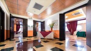 A hotel lobby with a check-in counter, seating area, and a large window with curtains. - West Point Airport Hotel (Villafranca di Verona)