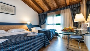 A hotel room with two beds, a glass table with fruit, a chair, and a desk with a lamp. - West Point Airport Hotel (Villafranca di Verona)