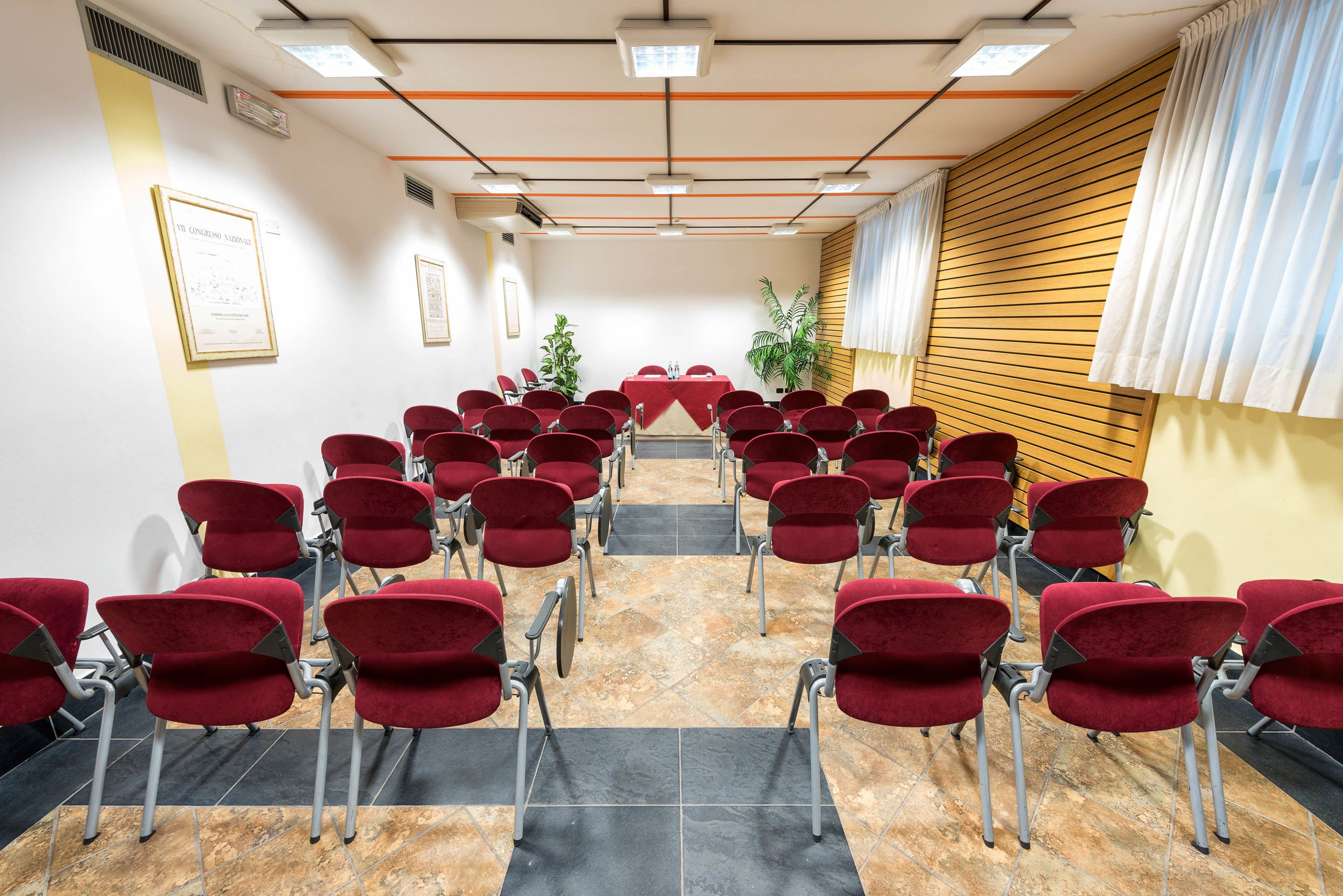 A conference room with red chairs arranged in rows, a table at the front, and framed certificates on the walls.