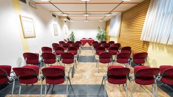 A conference room with red chairs arranged in rows, a table at the front, and framed certificates on the walls.