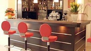 A bar area with a dark counter, red bar stools, hanging pendant lights, and a visible bar stocked with bottles. - Parkhotel Lindau (Lindau)