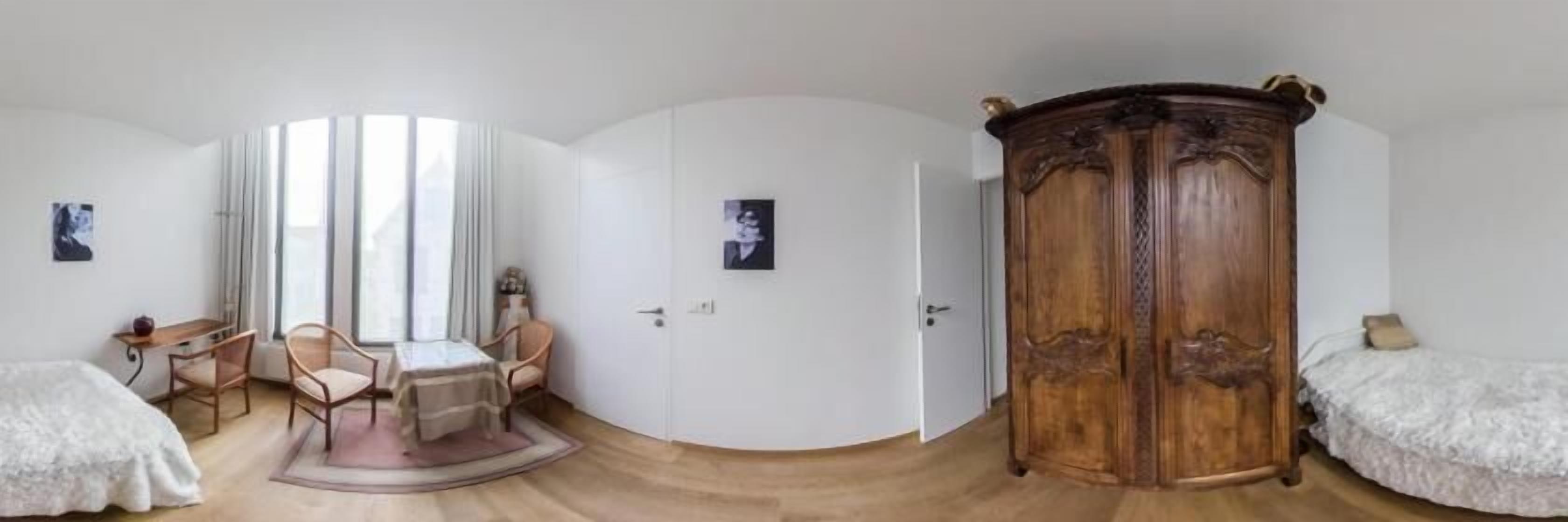 A room with a bed, a wooden wardrobe, a small table with chairs, and a door.