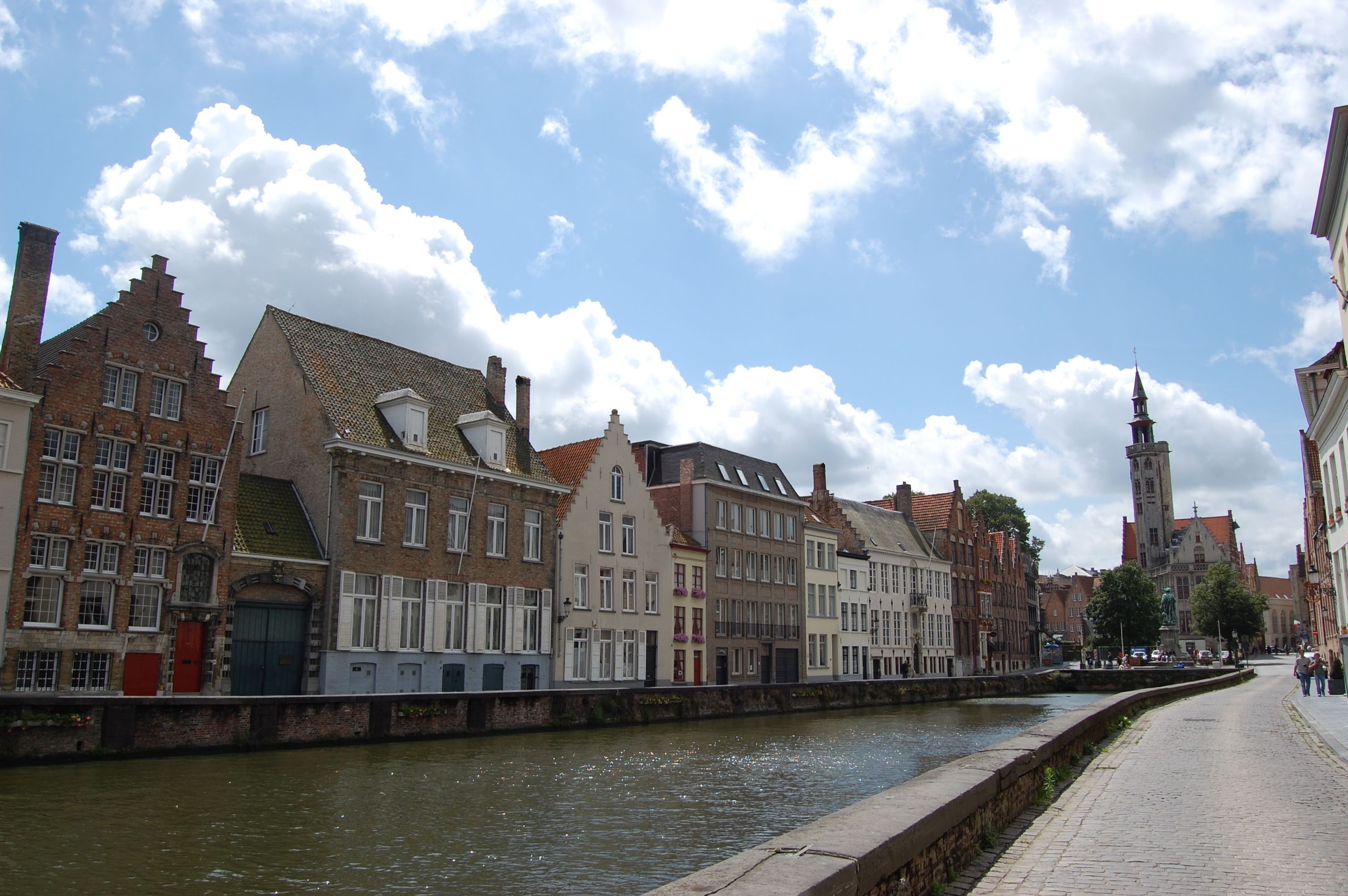 Een straat aan het water met historische gebouwen, een klokkentoren en een heldere lucht.