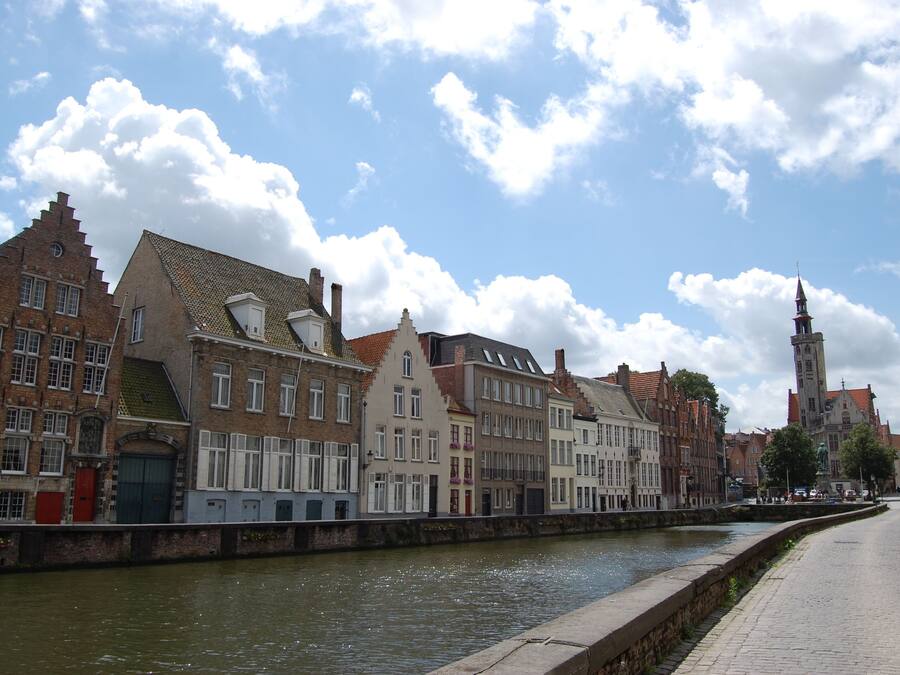 Een straat aan het water met historische gebouwen, een klokkentoren en een heldere lucht.