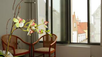 Une pièce avec une fenêtre donnant sur un immeuble, une chaise et un vase contenant des orchidées.