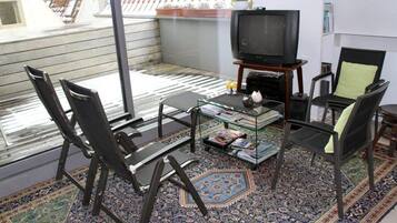 A small, cozy living room with a television, two chairs, a coffee table, and a bookshelf.