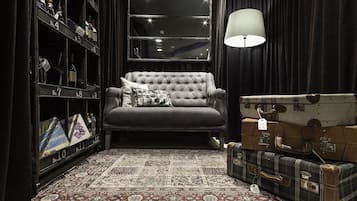 Een kamer met een gestoffeerde fauteuil, een kamerbreed tapijt met patroon, een boekenkast met genummerde vakken, en vintage koffers.