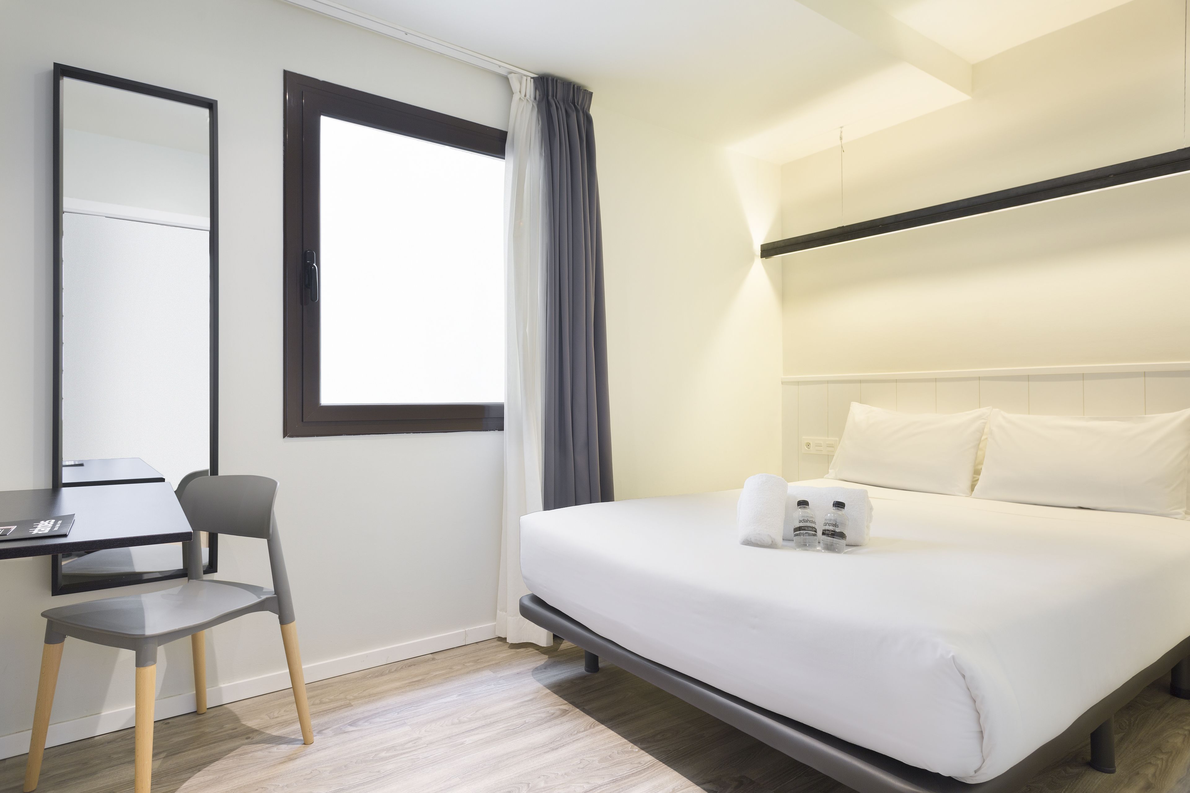 Een hotelkamer met een bed, een bureau, een stoel, een raam met gordijnen en een spiegel.