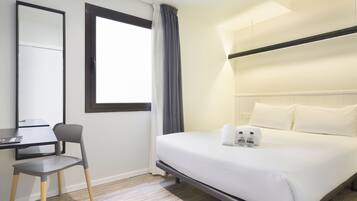 Een hotelkamer met een bed, een bureau, een stoel, een raam met gordijnen en een spiegel.
