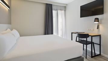 Habitación de hotel con una cama grande, un escritorio con silla, un televisor de pantalla plana en la pared y una ventana con cortinas.