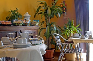 Uma área de refeições com uma mesa posta para dois, uma planta em vaso e um armário de madeira ao fundo.