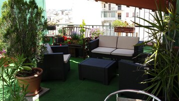 A balcony with wicker furniture, potted plants, and a view of the cityscape.