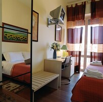 Una camera d'albergo con due letti, una scrivania con una sedia, una televisione e una finestra con tende.